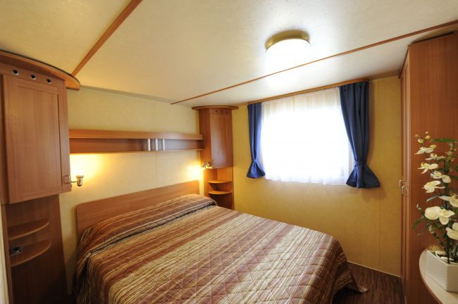 Una camera da letto con letto matrimoniale, mobili in legno chiaro e finestre con tende blu.