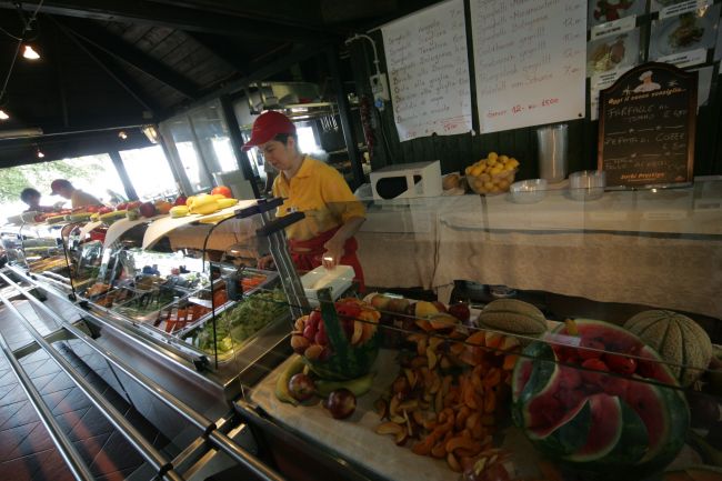 Un banco self-service con frutta fresca e insalate, gestito da un dipendente in divisa.
