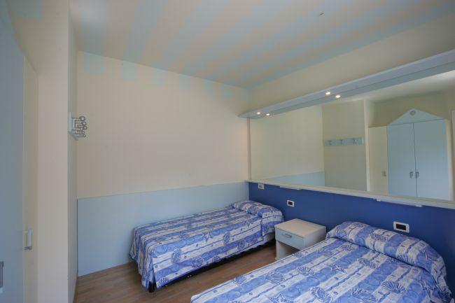 Due letti singoli con copriletti blu in una stanza con specchio e armadio.
