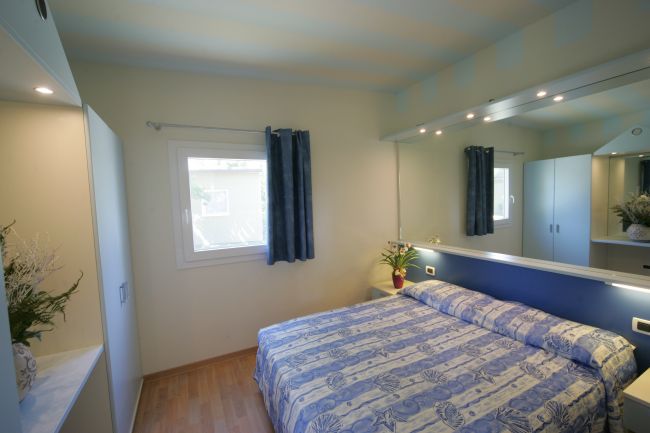 Letto matrimoniale con copriletto blu, specchio, finestra e armadio.