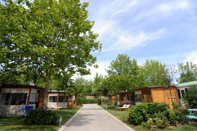Case mobili con giardino e alberi su una strada asfaltata sotto un cielo blu.