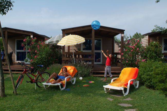 Due bambini in un giardino con lettini e bici, davanti a bungalow.