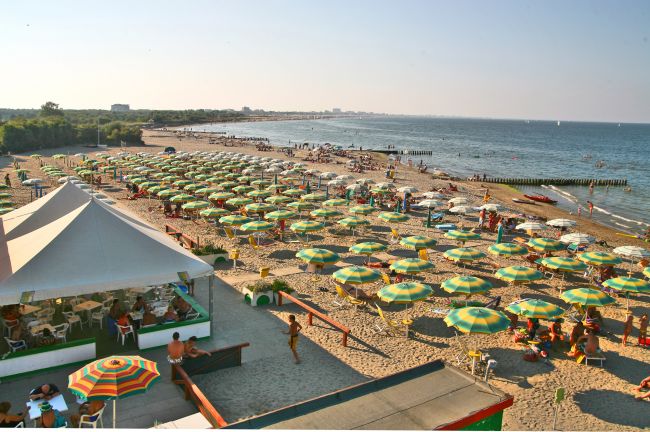 Spiaggia con file di ombrelloni verdi e gialli vicino al mare.