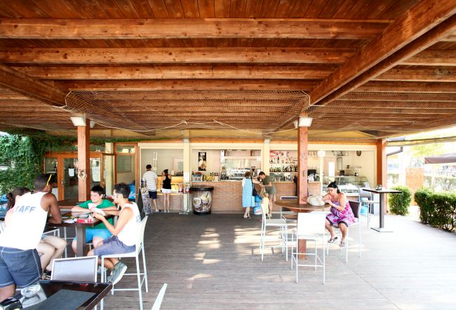 Bar all'aperto con persone sedute ai tavoli e un bancone.