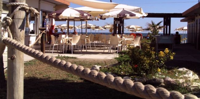 Bar all'aperto con tavoli, sedie e ombrelloni.