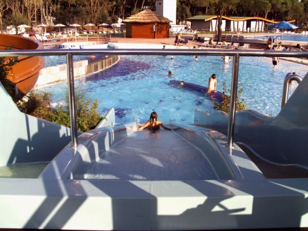 Una persona scivola giù da uno scivolo verso una piscina affollata.