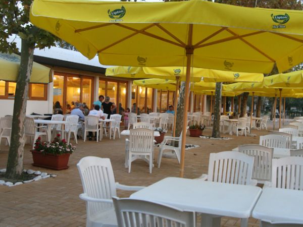 Terrazza di un bar con sedie bianche e ombrelloni gialli.
