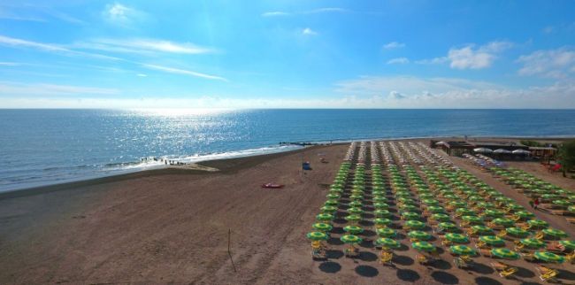 Ampia spiaggia con ombrelloni gialli e mare calmo.