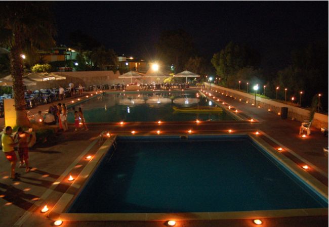 Piscina illuminata di notte con luci intorno.