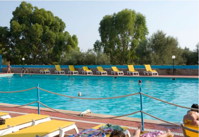 Piscina con lettini gialli e alberi sullo sfondo.
