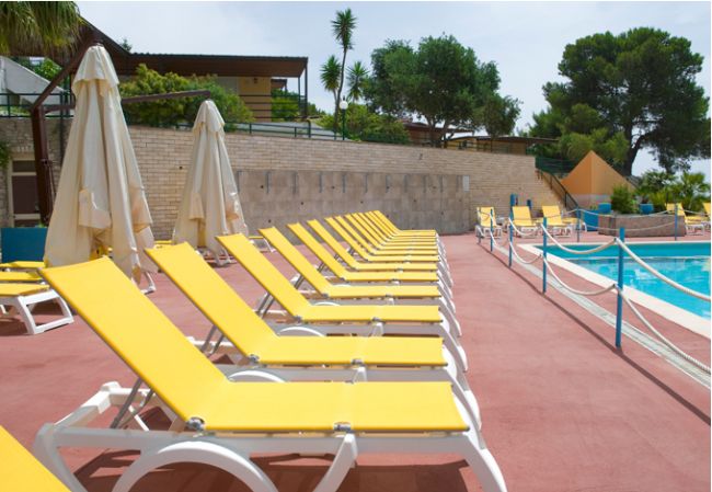 File di lettini gialli lungo una piscina con ombrelloni bianchi.