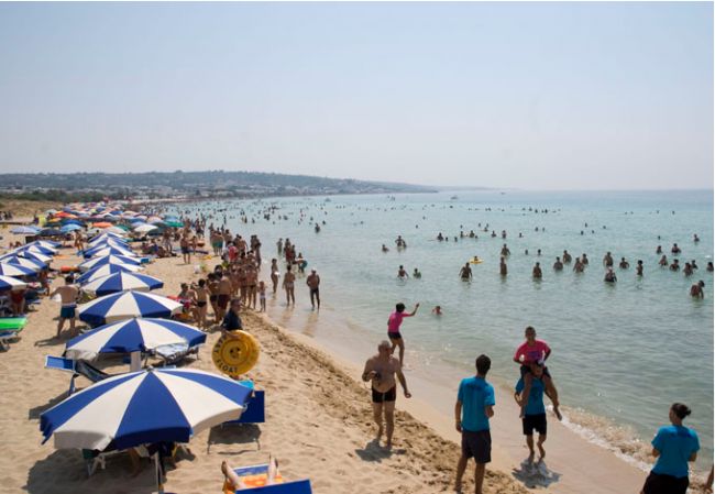Spiaggia affollata con ombrelloni blu e bianchi.
