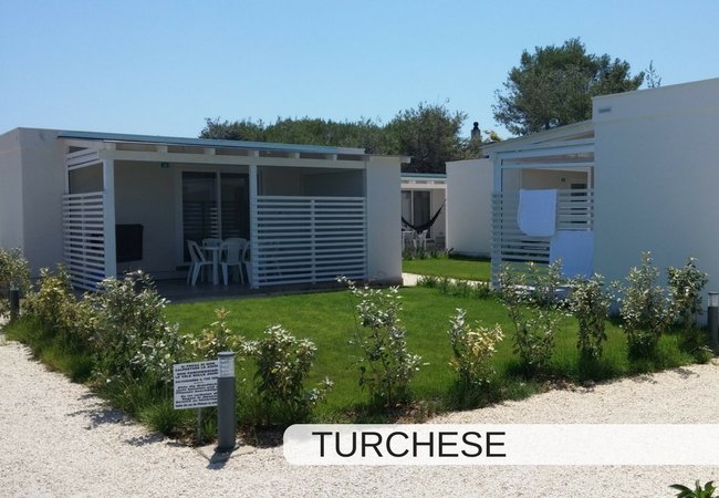 Due bungalow bianchi con giardino e sedie fuori.
