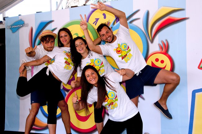 Cinque persone posano sorridenti con sfondo colorato.