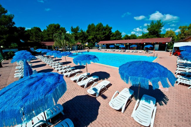 Piscina con ombrelloni blu e lettini bianchi.