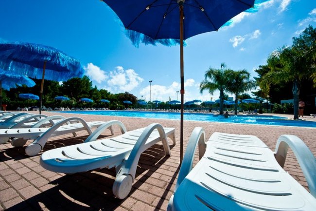 Lettini bianchi sotto ombrelloni blu vicino alla piscina.