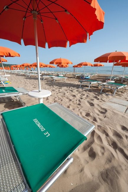 Spiaggia sabbiosa con lettini verdi e ombrelloni arancioni.