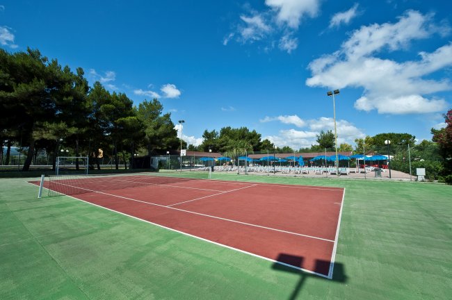 Campo da tennis vuoto con un cielo blu e alberi sullo sfondo.