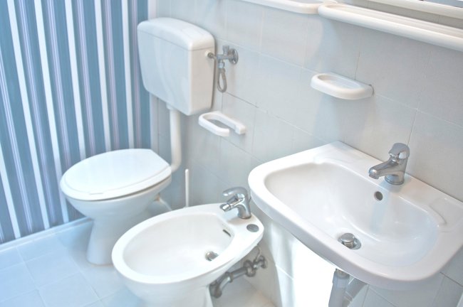 Un bagno con WC, bidet e lavabo bianchi su fondo a righe blu.