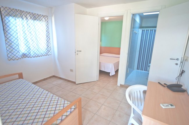 Una stanza con letto singolo, scrivania e porta che conduce a un bagno.