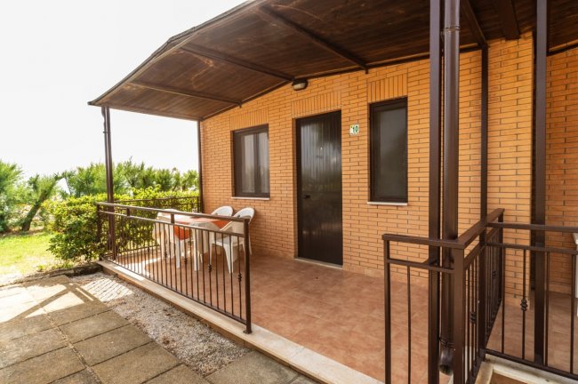 Veranda esterna con sedie e tavolo sotto una tettoia.
