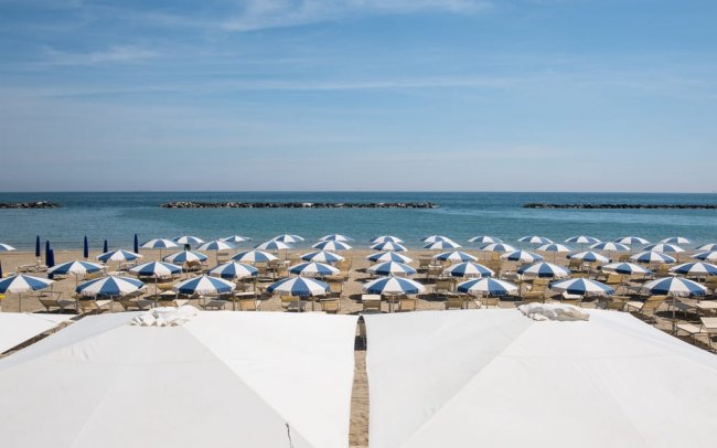 Spiaggia con file di ombrelloni blu e bianchi.