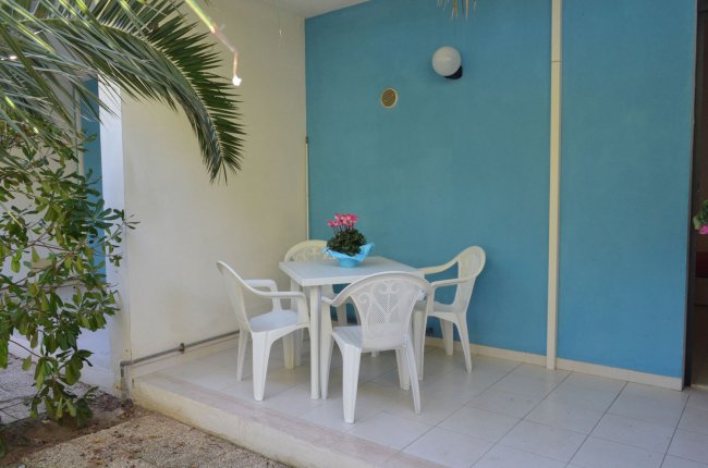 Tavolino esterno con sedie bianche e parete blu.