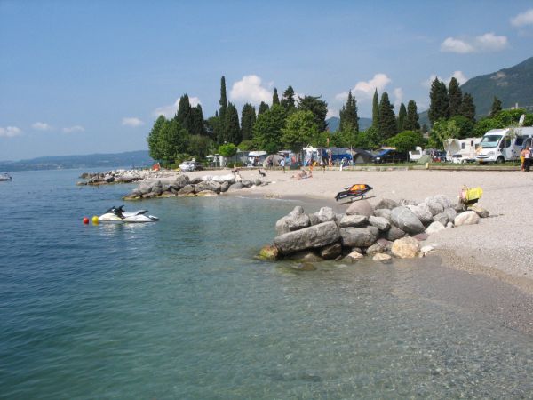 Una spiaggia di ciottoli con acqua limpida, rocce e jet ski.